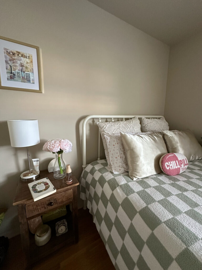 bedroom with made bed, side table with book, flowers, lamp